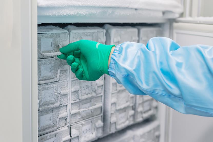 green gloved hand reaching into refrigerator freezer unit and touching handle of metal box 