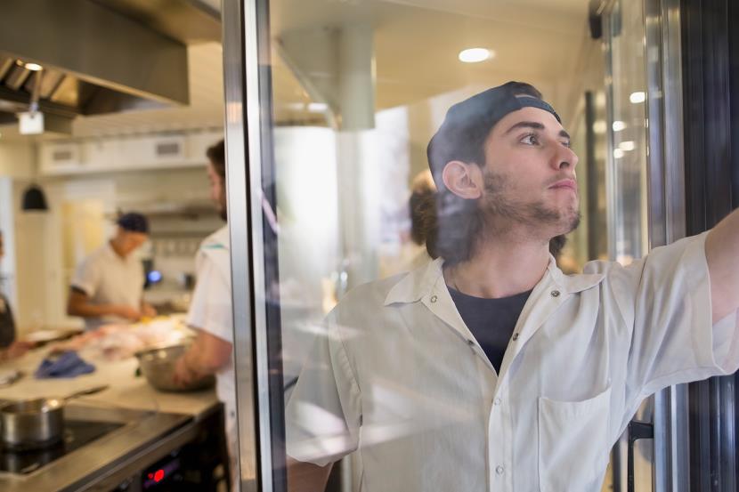 man in commercial restaurant kitchen reaching into a refrigerator