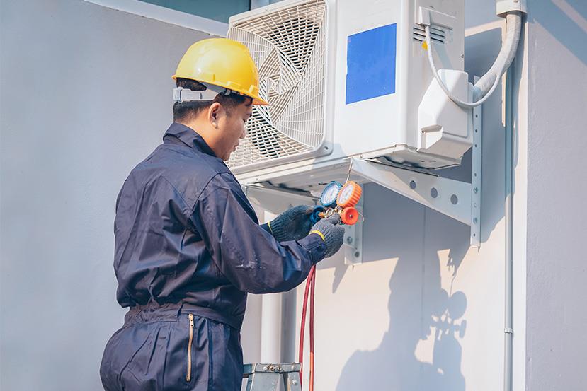 technician holding orange and blue vacuum pump while checking outdoor air conditioning unit